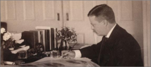 Black and white photograph of Theodore Roosevelt writing a letter at his desk.