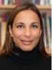 Headshot of Shirley Moody Turner. A smiling woman with straight brown hair wearing a black turtleneck, standing in front of a bookshelf.